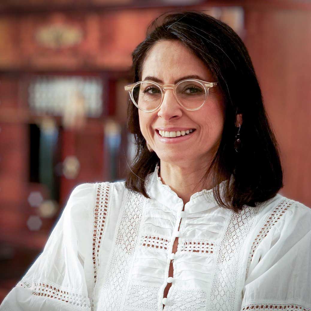 Asli Demirel, Systemische Therapeutin und Heilpraktikerin f&uuml;r Psychotherapie, l&auml;chelnd, sitzend an ihrem Schreibtisch in Berlin Mariendorf, in wei&szlig;em Kleid und durchsichtiger Brille.