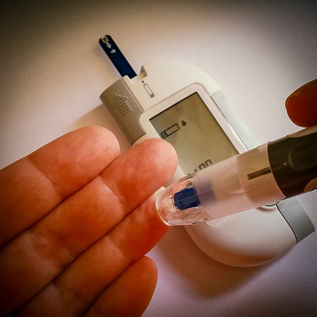 Foto eines Blutzuckermessger&auml;ts und einer Stechhilfe bei der Abnheme von Kapillarblut am Finger.