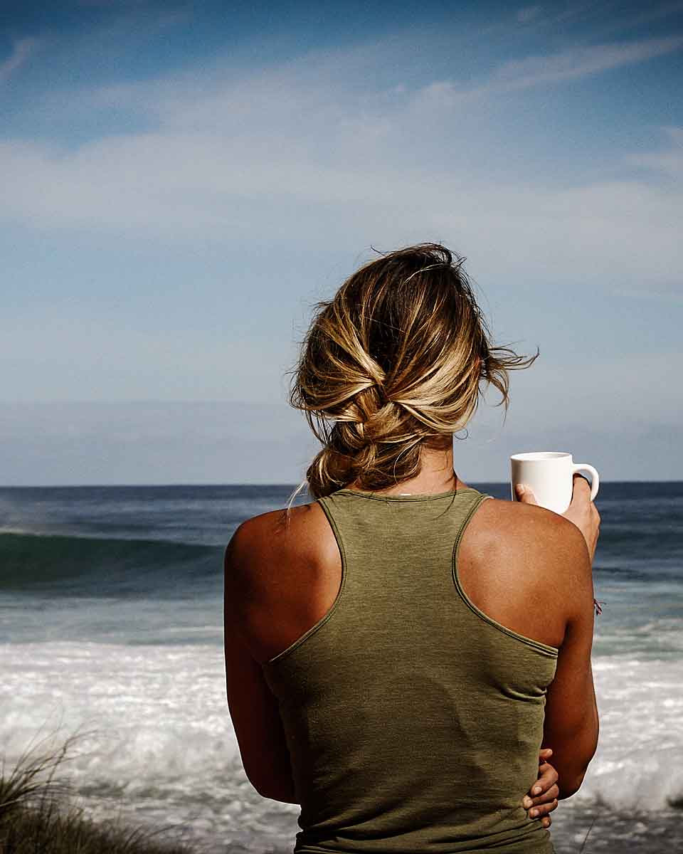Eine Frau mit einer Kaffeetasse in der Hand schaut auf das Meer an einem schönen Sommertag. Sie denkt nach die Schwerpunkte, die sie mit Asli Demirel in ihrer letzten Coaching Session durchgeführt hat.